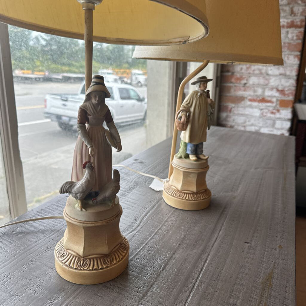 Two lamps with figurines on a wooden surface, one with a yellow lampshade.