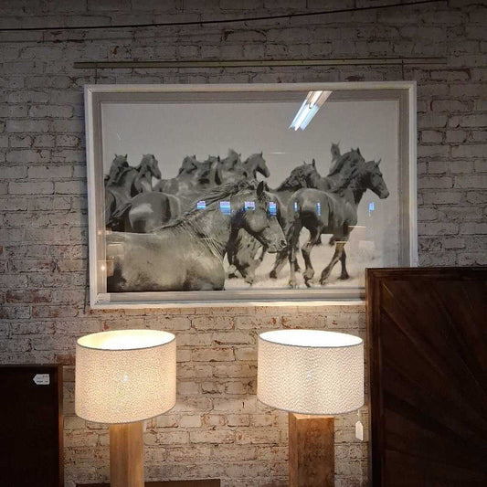 Framed artwork of horses running on a brick wall with two lamps below.