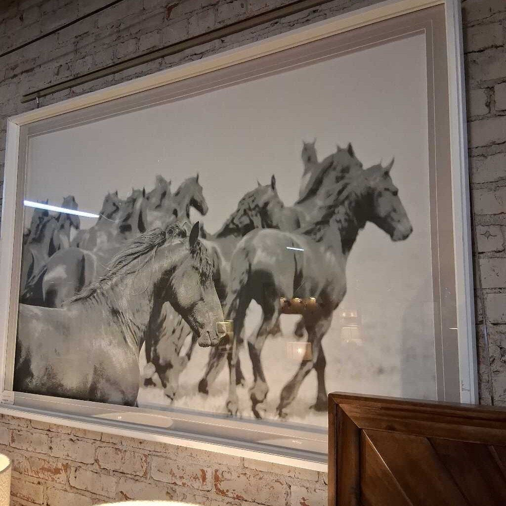 Framed artwork of horses running on a textured wall.