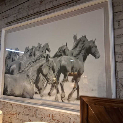 Framed artwork of horses running on a textured wall.