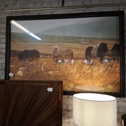 Framed photograph of horses in a field on a brick wall.