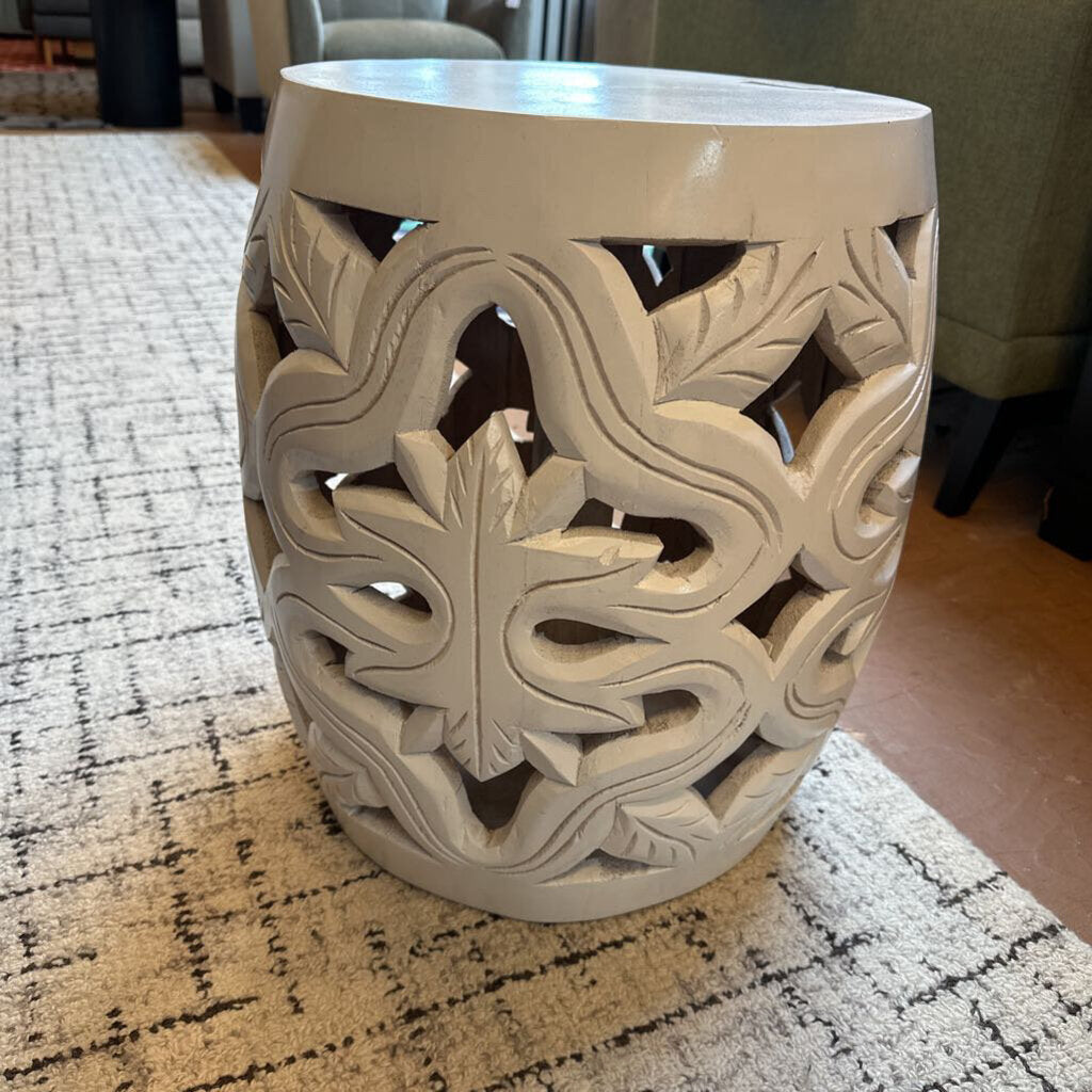 Decorative white ceramic stool with intricate cut-out patterns on a textured rug.
