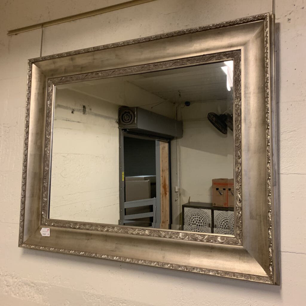 Silver framed mirror on a wall with a room reflection