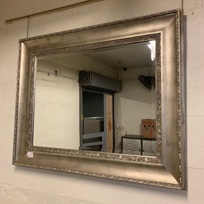 Silver framed mirror on a wall with a room reflection