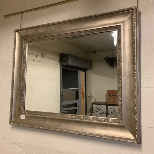 Silver framed mirror on a wall with a room reflection