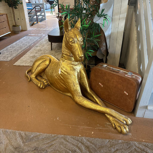 Gold dog statue next to a brown suitcase on a wooden floor.