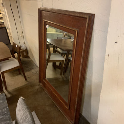 Wooden framed mirror leaning against a wall in a room with furniture.