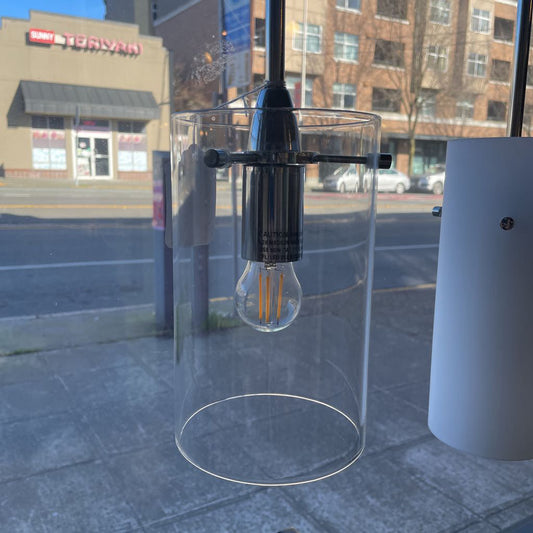 Clear cylindrical container with a light bulb inside on a city street.