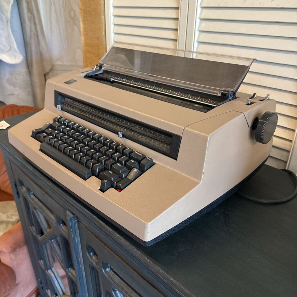 Beige typewriter on a surface with a window in the background