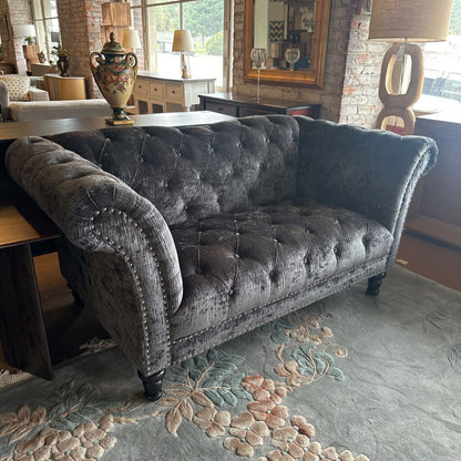 Gray tufted sofa in a room with a brick wall and decorative rug.
