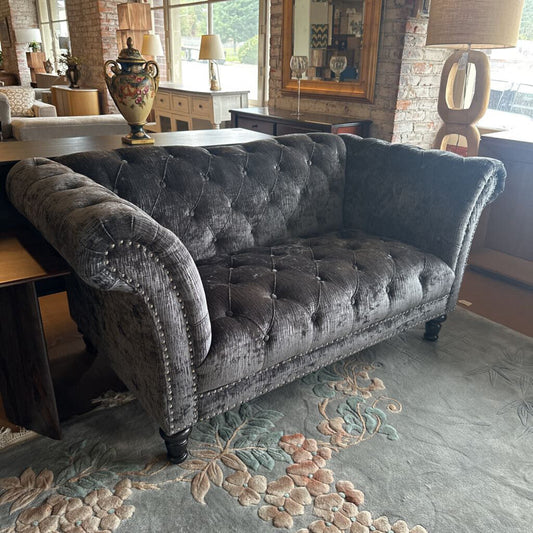 Gray tufted sofa in a room with a brick wall and decorative rug.