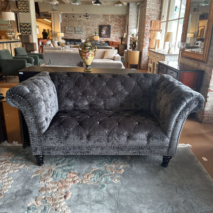 Gray tufted sofa in a showroom with other furniture and decor.