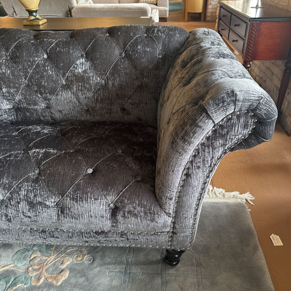 Gray tufted sofa in a room with a patterned rug and wooden floor.