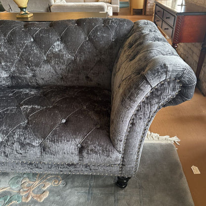 Gray tufted sofa in a room with a patterned rug and wooden floor.
