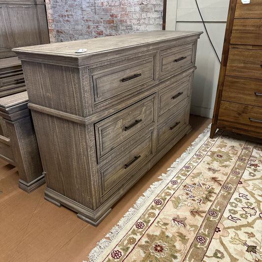 Wooden dresser with multiple drawers on a wooden floor with a patterned rug.