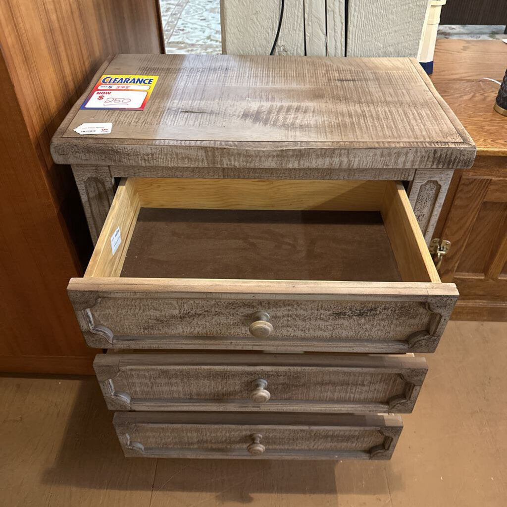Wooden nightstand with open drawer and 'Clearance' sign on top, against a wooden wall.