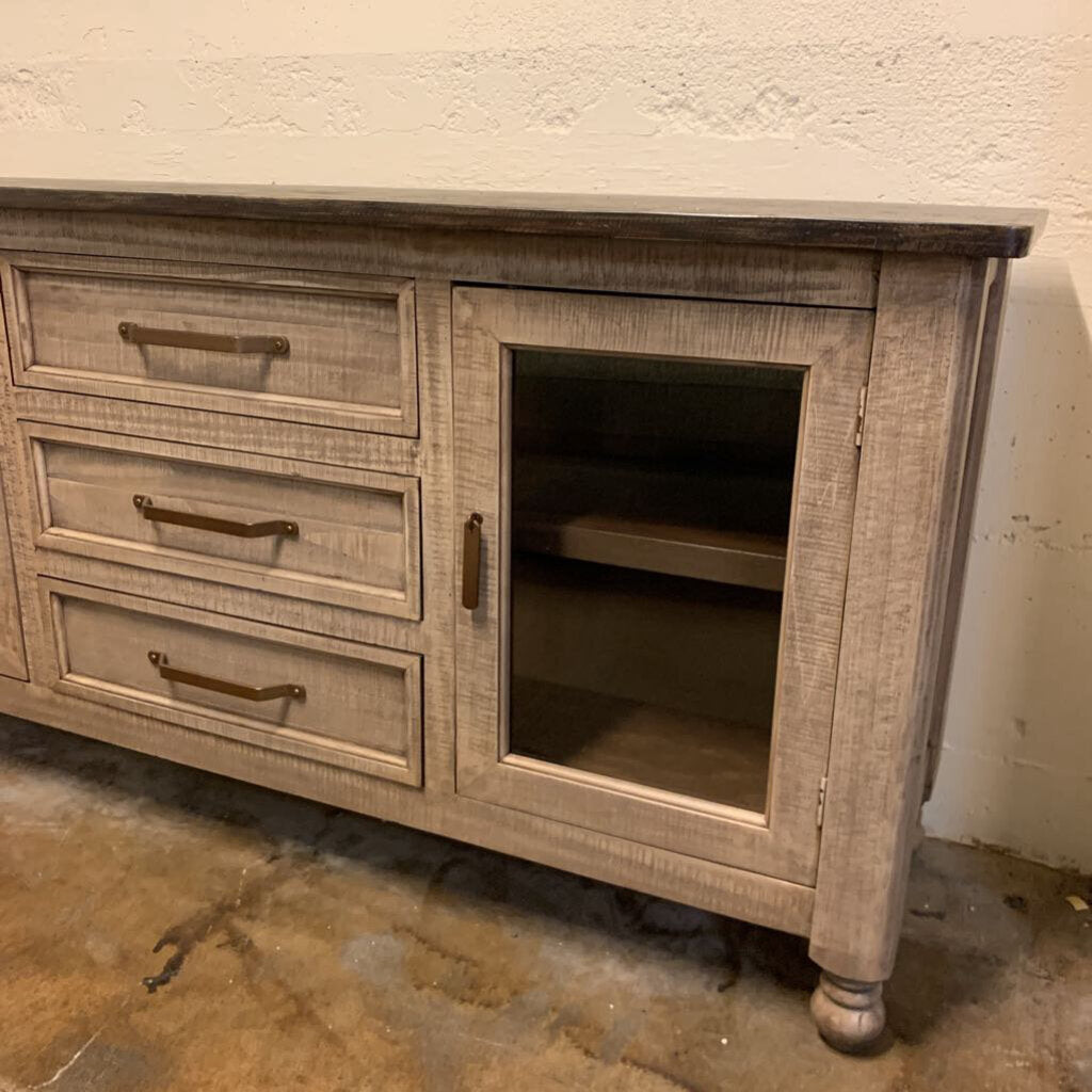 Wooden dresser with drawers and a cabinet door in a room with a textured wall and concrete floor.