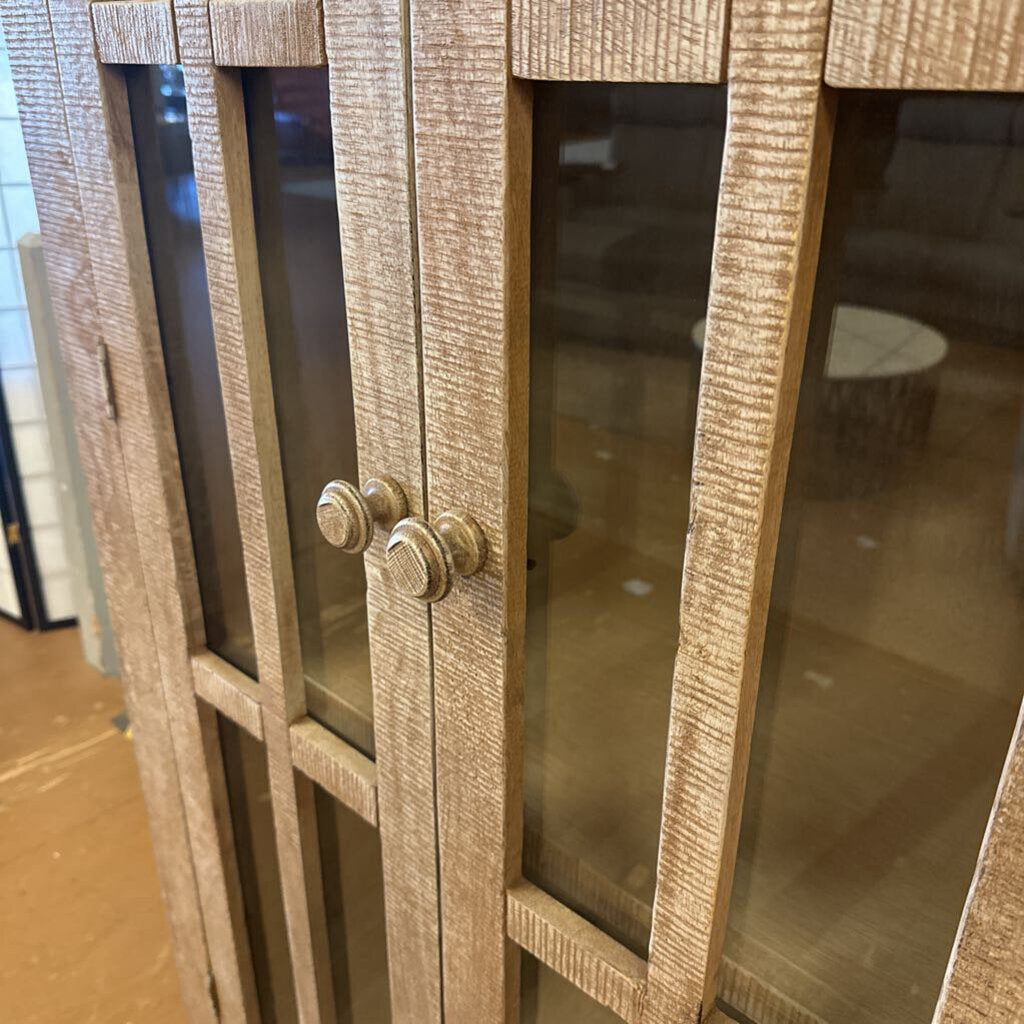 Wooden cabinet with glass doors and metal handles in a room setting.