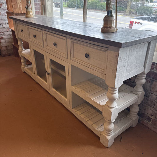White wooden console table with black top in a room with brick walls and a window.