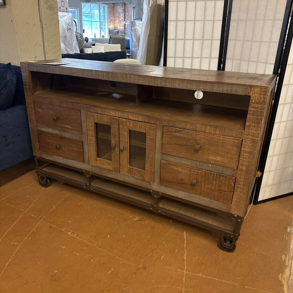 Wooden entertainment console with glass doors and drawers in a room setting.