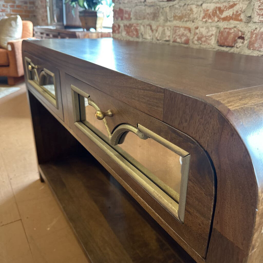 Wooden console table with glass panels and brass handles in a room with brick wall.