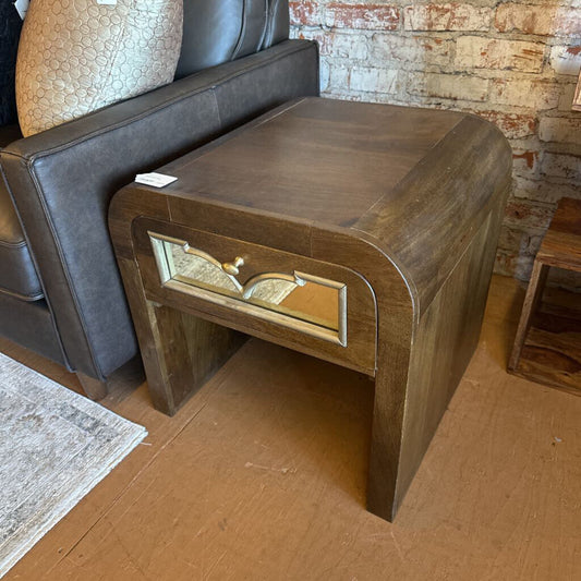 Wooden side table with gold accents in a room with a sofa and brick wall.
