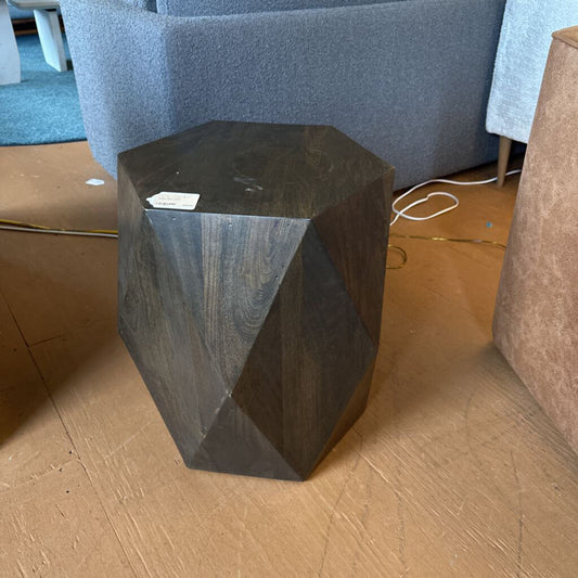 Hexagonal dark wood side table on a wooden floor with furniture in the background
