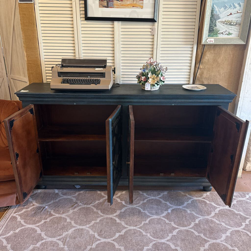 Dark wooden cabinet with open doors, featuring a typewriter and decorative items on top, in a room with a patterned rug and framed pictures on the wall.