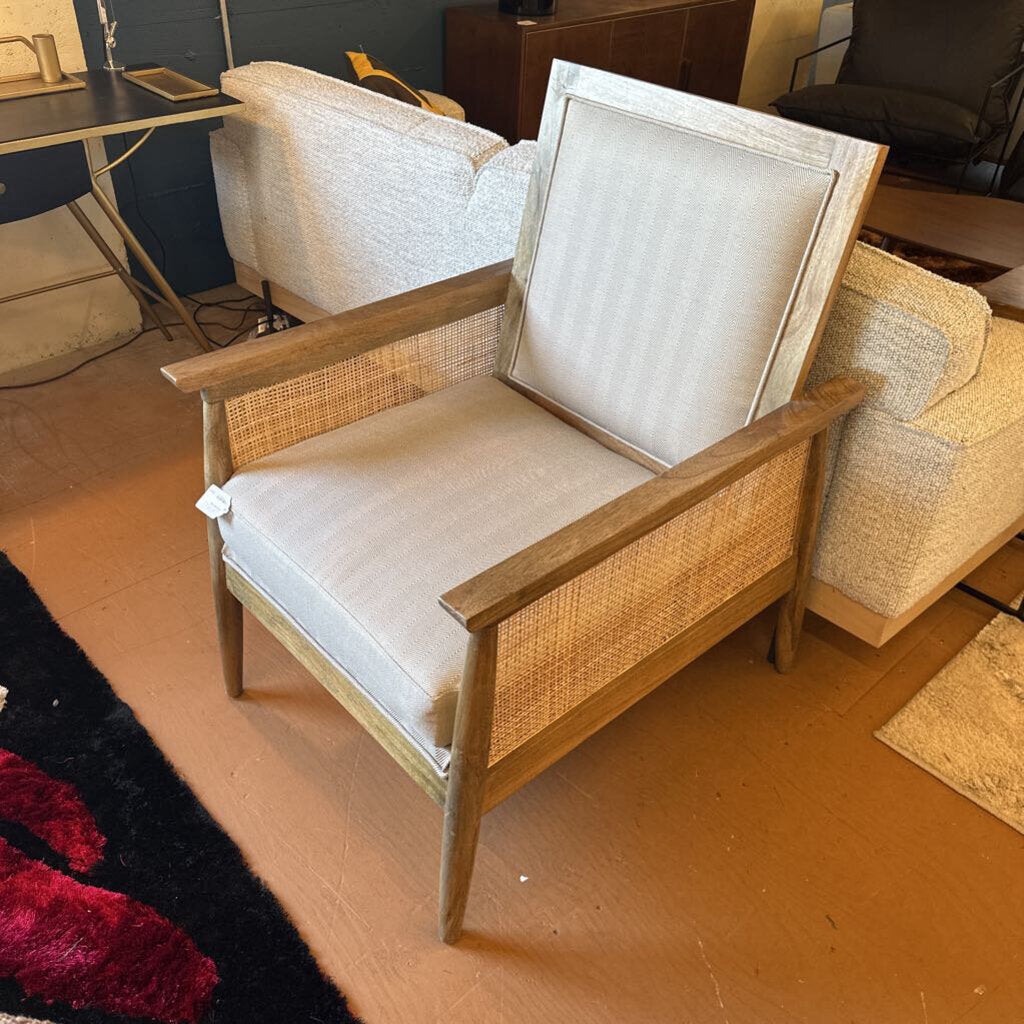 Wooden armchair with wicker backrest and beige cushion on a wooden floor.