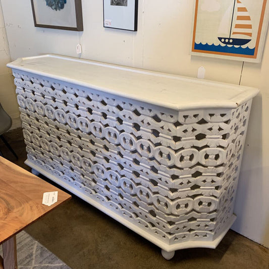 Decorative white lattice cabinet in a room with framed artwork on the wall.