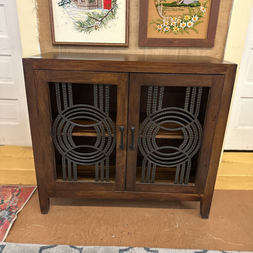 Wooden cabinet with decorative metal grilles on a wooden floor.