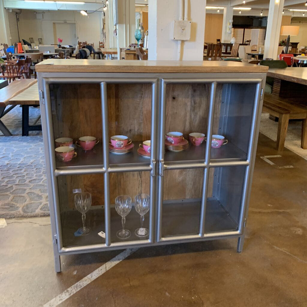 Cabinet with glass doors displaying various items in a room with tables and chairs.