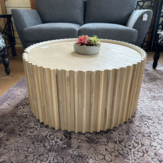 Round wooden coffee table with a textured surface in a room with a gray sofa and patterned rug.