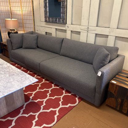 Gray sofa in a room with a red patterned rug and wooden floor.