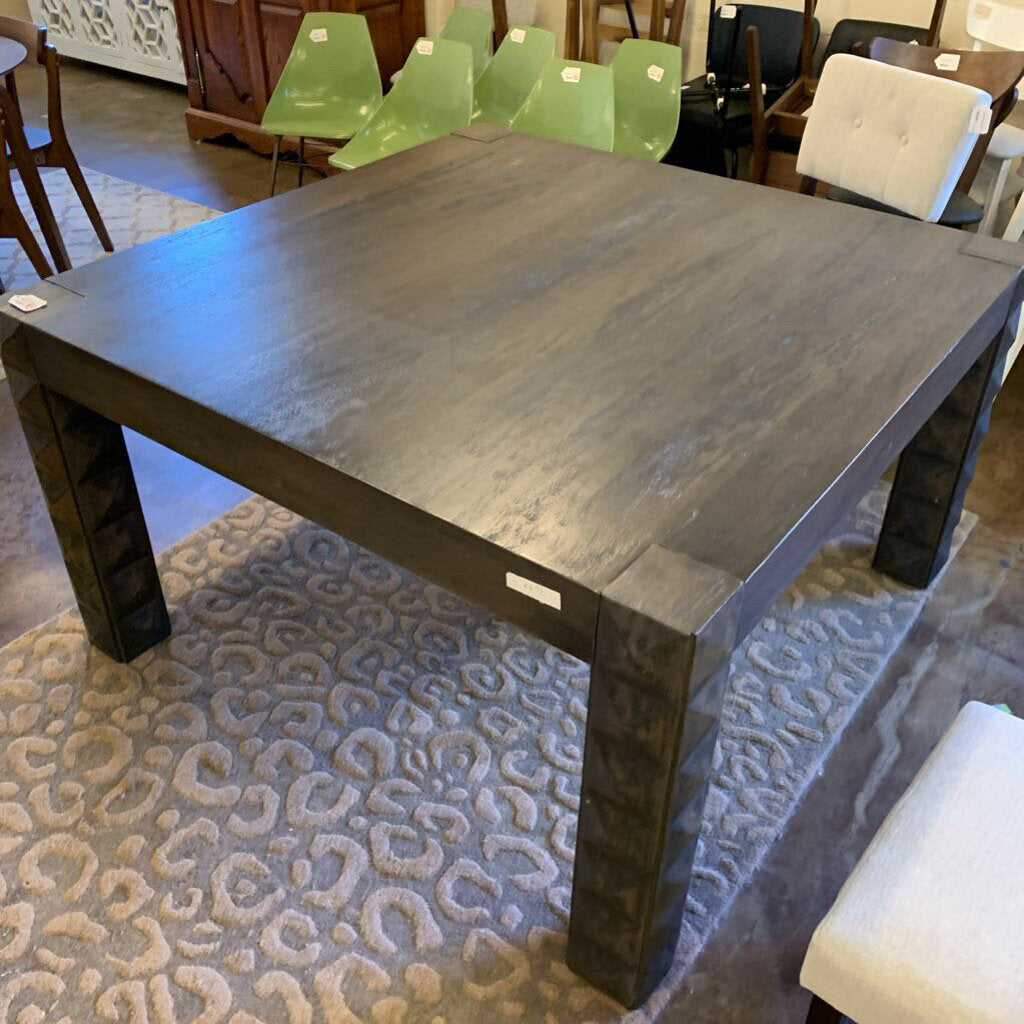 Dark wooden dining table in a showroom setting with chairs around it.