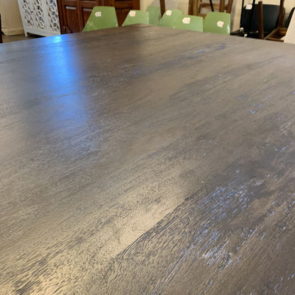 Large wooden dining table with a smooth finish, surrounded by green chairs.