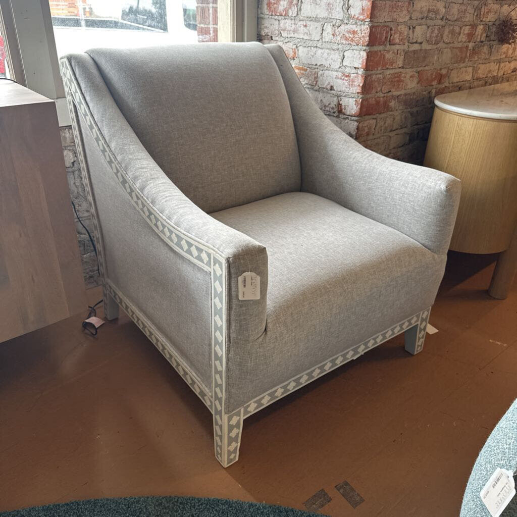 Gray armchair in a room with a brick wall and wooden floor.
