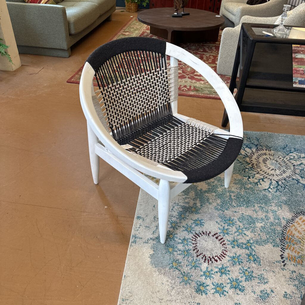 Wicker chair with black woven seat on a patterned rug in a living room setting