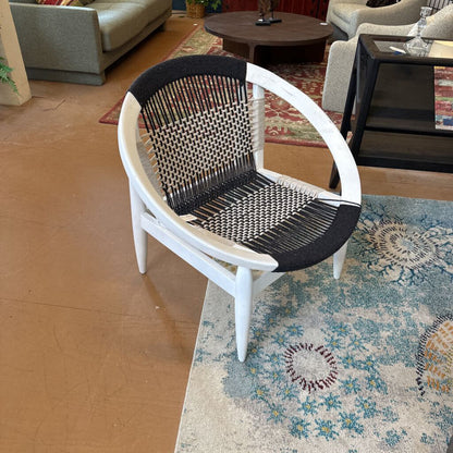 Wicker chair with black woven seat on a patterned rug in a living room setting