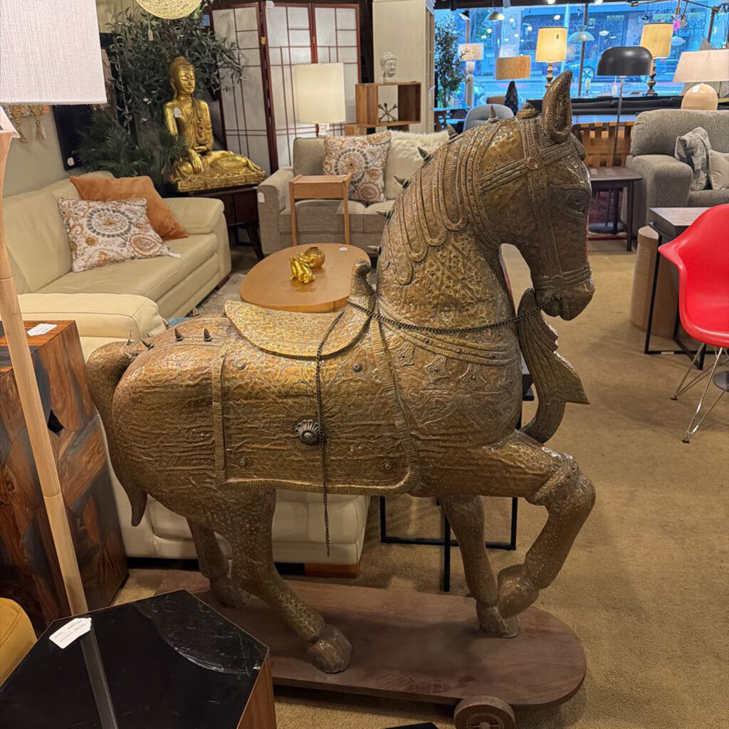 This monumental Indian-style Ashva horse statue is a masterwork of decorative craftsmanship, designed to serve as a grand focal point in a high-end interior. The statue is finished in a highly detailed antiqued brass or bronze-toned metal, featuring intricate embossed patterns that mimic traditional ceremonial armor and tack.