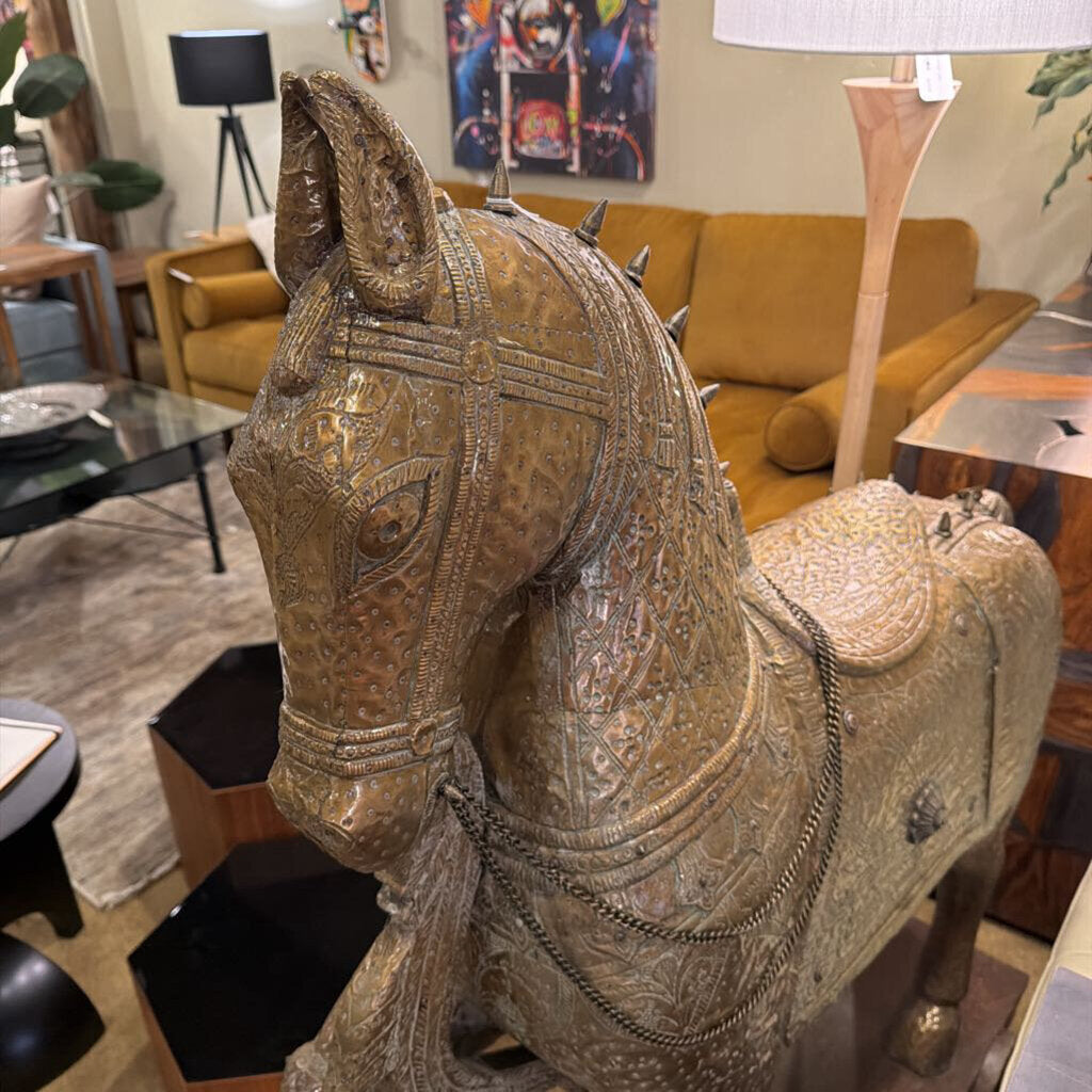 This monumental Indian-style Ashva horse statue is a masterwork of decorative craftsmanship, designed to serve as a grand focal point in a high-end interior. The statue is finished in a highly detailed antiqued brass or bronze-toned metal, featuring intricate embossed patterns that mimic traditional ceremonial armor and tack.