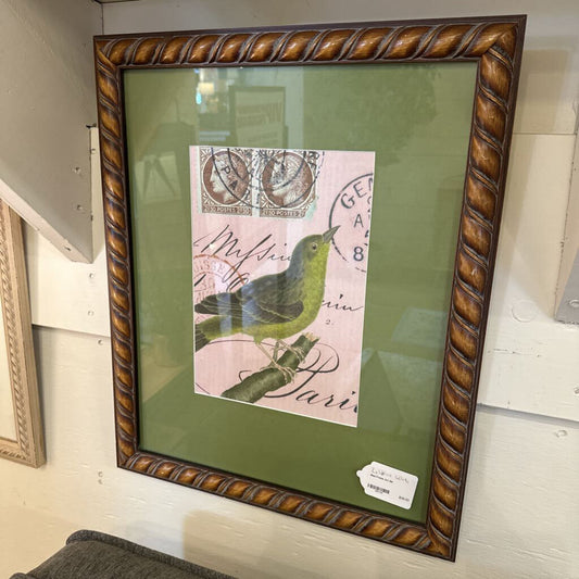 Framed artwork with a green bird illustration on a pink background, displayed on a wall.