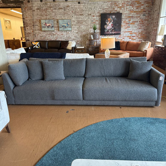 Gray sofa in a living room setting with a brick wall and various decor items.
