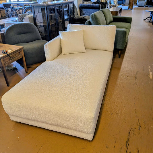 White textured chaise lounge with a pillow on a wooden floor in a furniture store.