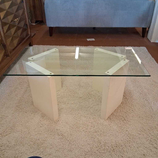 Glass coffee table on a beige carpet with a blue ottoman in the background