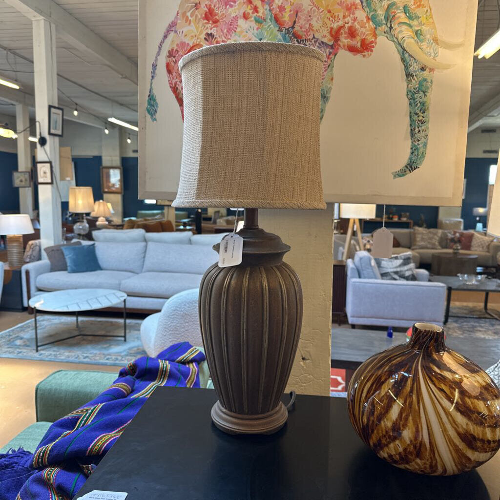 Decorative lamp with a beige shade on a table in a furniture store setting.