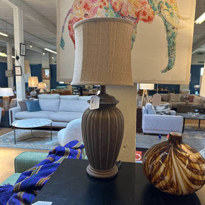 Decorative lamp with a beige shade on a table in a furniture store setting.