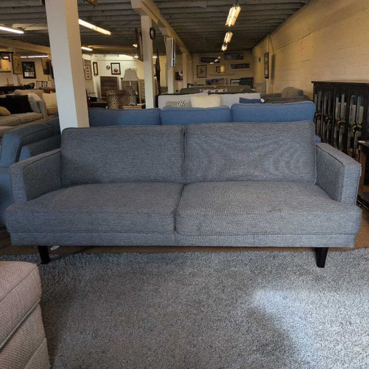 Gray sofa in a furniture store setting with other furniture items in the background.