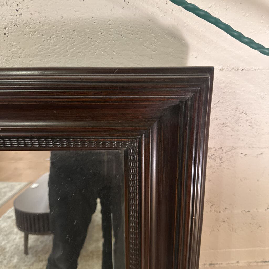 Close-up of a dark wooden mirror frame against a light-colored wall.