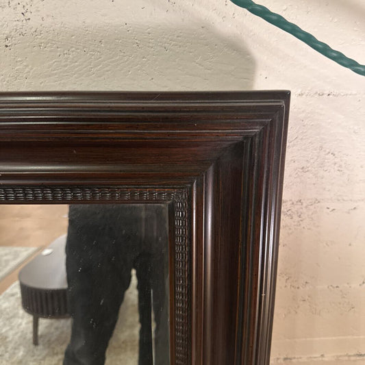 Close-up of a dark wooden mirror frame against a light-colored wall.